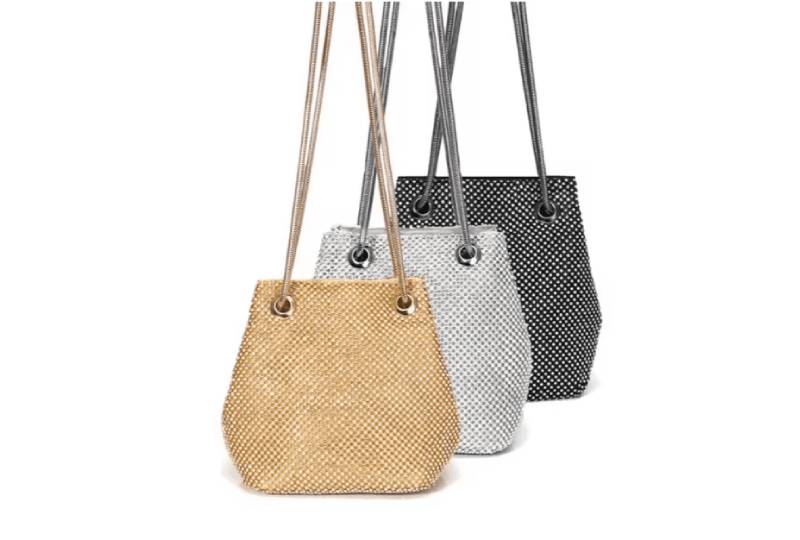 Three woven bucket bags in beige, white, and black with long straps.