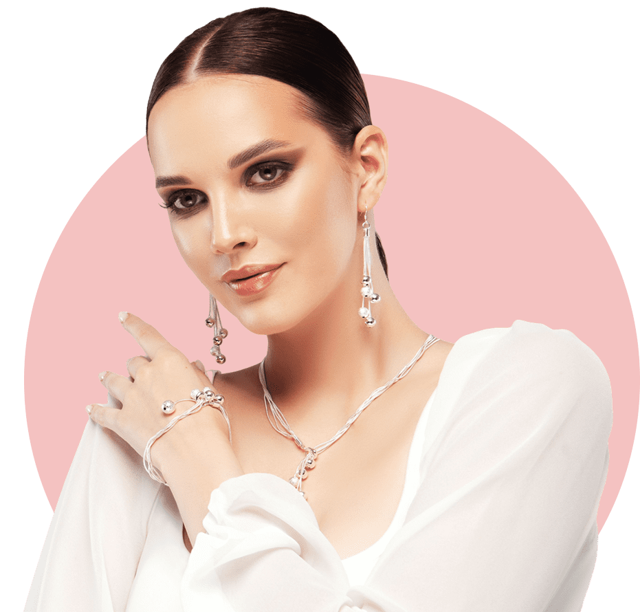 Elegant woman with delicate jewelry and soft makeup against pink background.