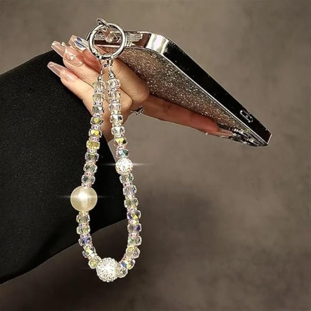 A phone with a beaded pearl and crystal charm strap attached.